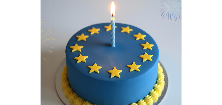 Runder blauer Kuchen mit gelben Sternen in einem Kreis angeordnet, dekoriert wie die Europaflagge, mit einer einzelnen brennenden Kerze in der Mitte